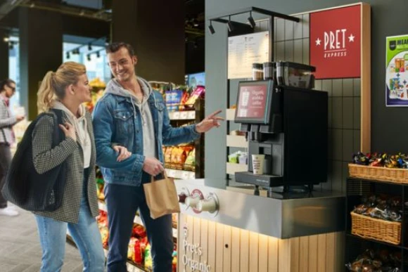 two people in casual clothes selecting a drink from a pret express unit in a forecourt store